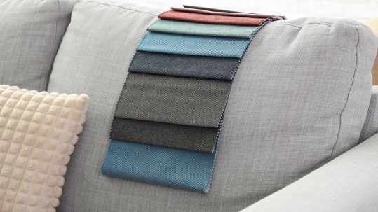 Upholstery fabric swatches in multiple colors laid on gray sofa