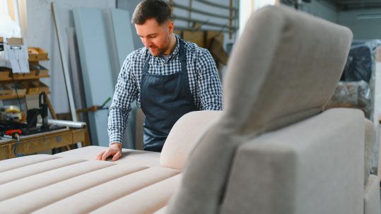 Upholstery craftsman smoothing fabric on sofa in workshop